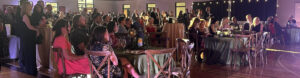 A wide shot of the crowd from the Meadow to the Mountain event at Rundle. People sit and stand in the gymnasium listening to a speaker