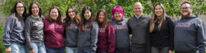 A photo of 10 Rundle Studio teachers wearing Rundle-branded clothing posing for a photo in front of green foliage.